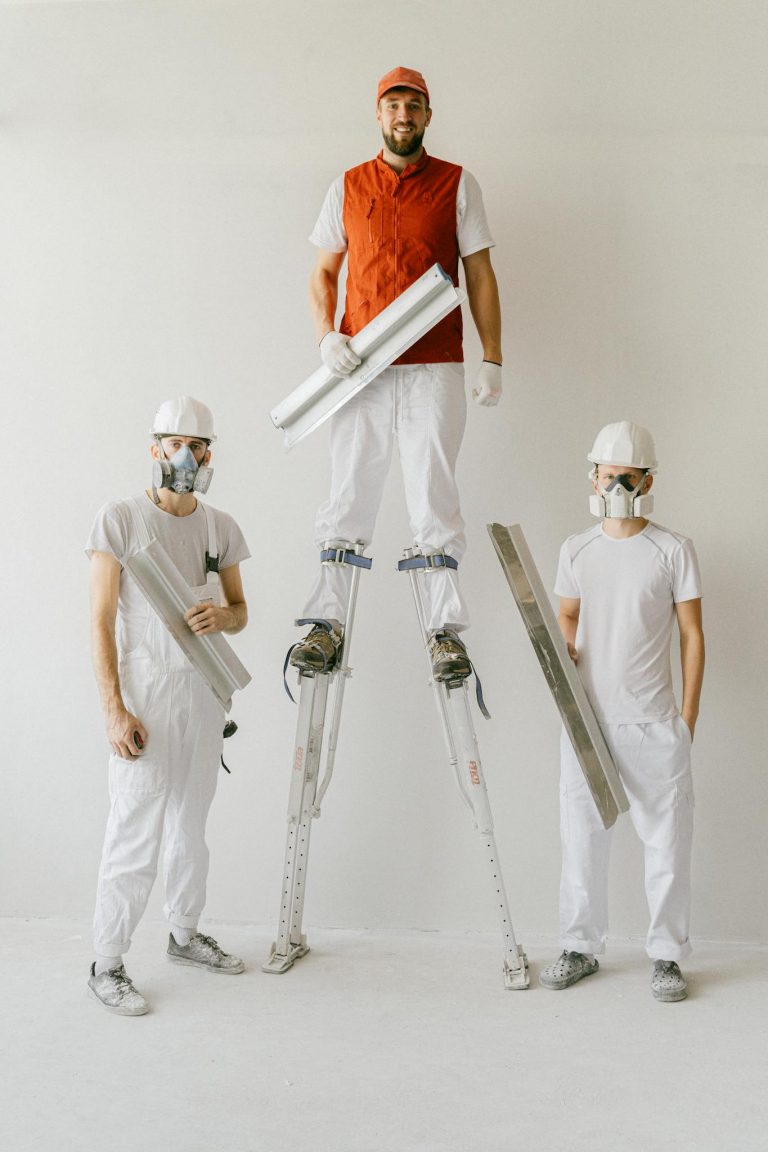 Construction workers in uniforms and hard hats using drywall stilts indoors.