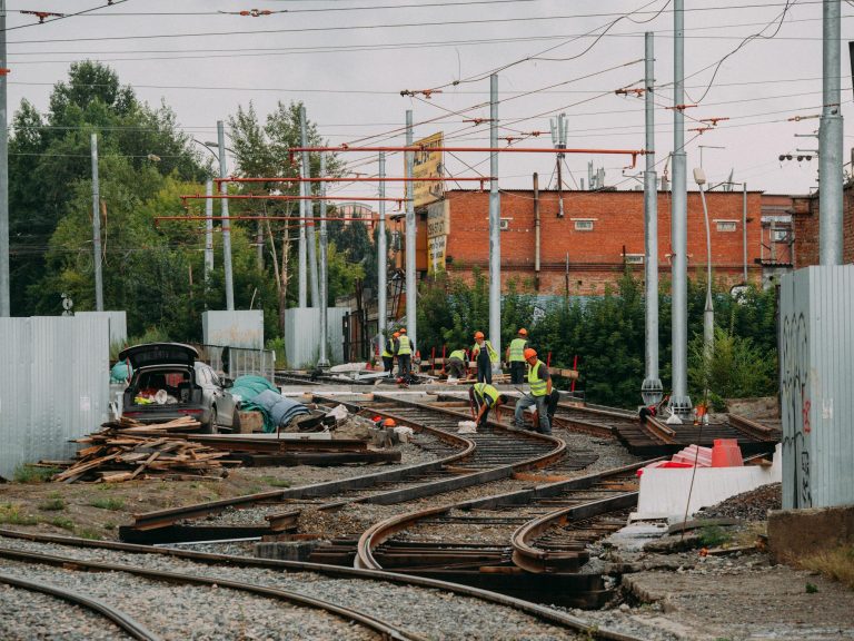 Workers repairing train tracks outdoors amidst an urban setting, emphasizing industry and teamwork.